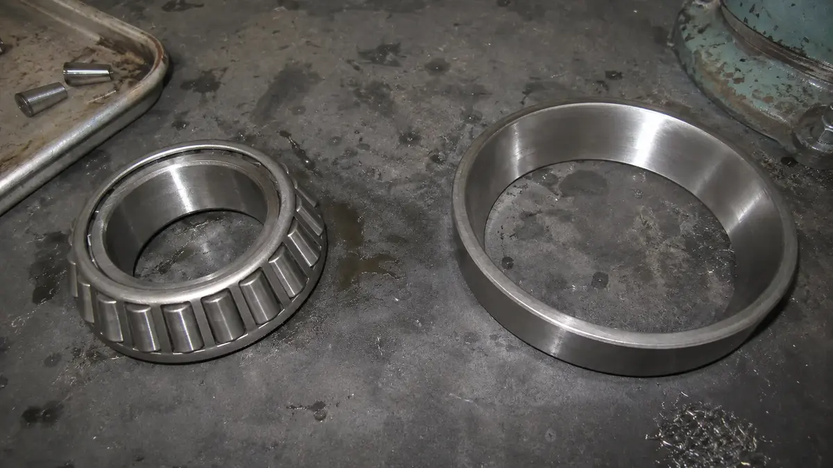 A tapered roller bearing lying in its two separately ordered halves: on the left the cone assembly with its inner ring, tapered rollers, cage and large-end rib, and on the right the cup as a bare outer ring with a plain conical bore, which is why an interchange that returns one number has returned half an assembly