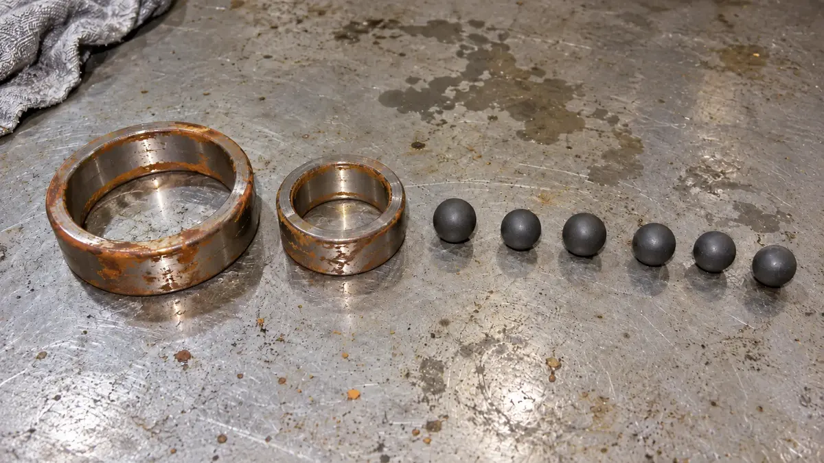 Steel inner and outer rings of a hybrid ceramic bearing covered in patchy orange surface rust, laid out beside six clean silicon nitride balls showing no corrosion, because only the steel rings of a hybrid bearing can rust