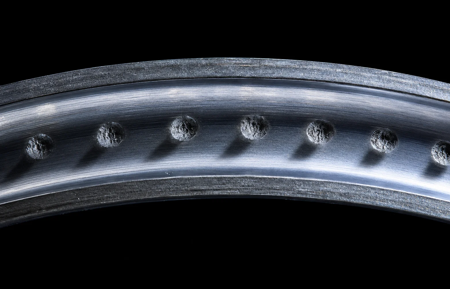Macro photograph of a bearing inner-ring raceway showing a row of evenly-spaced ball-shaped indentations from a static-overload brinelling event